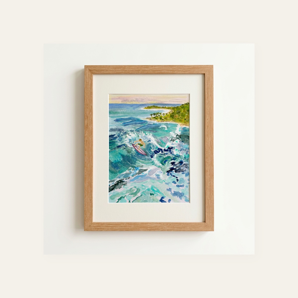 Framed watercolor of a lone surfer riding a turquoise wave near a tropical cove at sunset