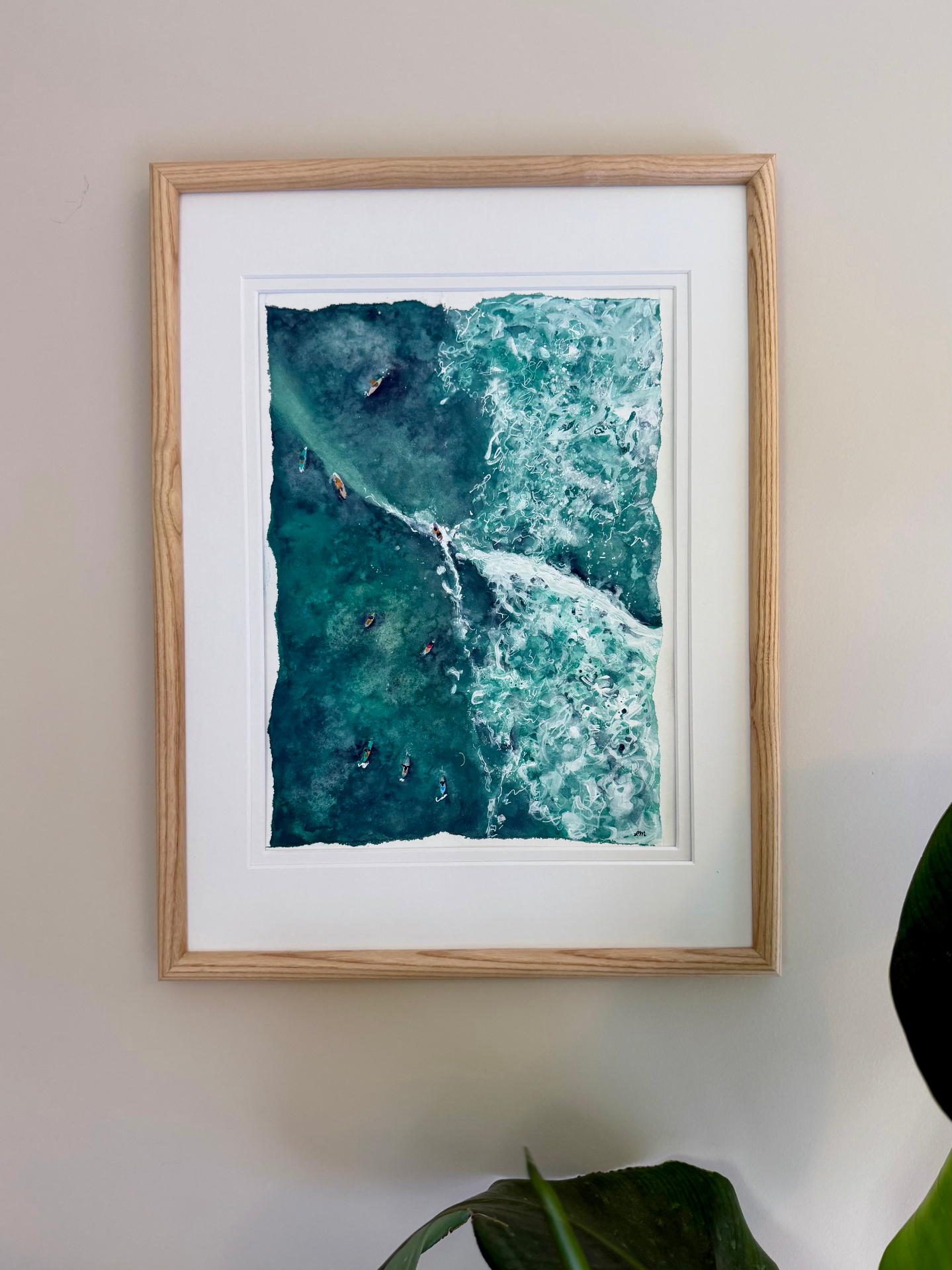 Framed watercolor of surfers paddling out through a turquoise wave from above
