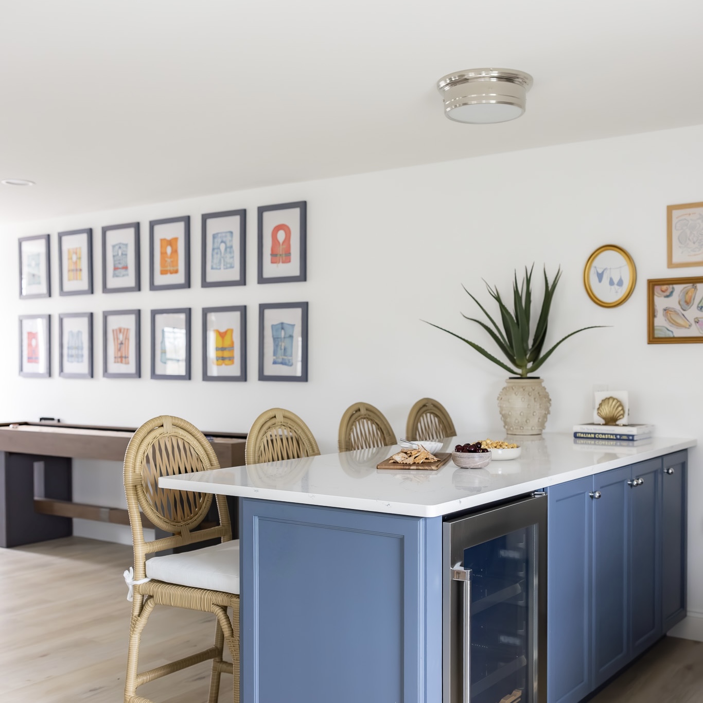 Life vest watercolor series displayed on a wall beside a blue kitchen island with rattan stools
