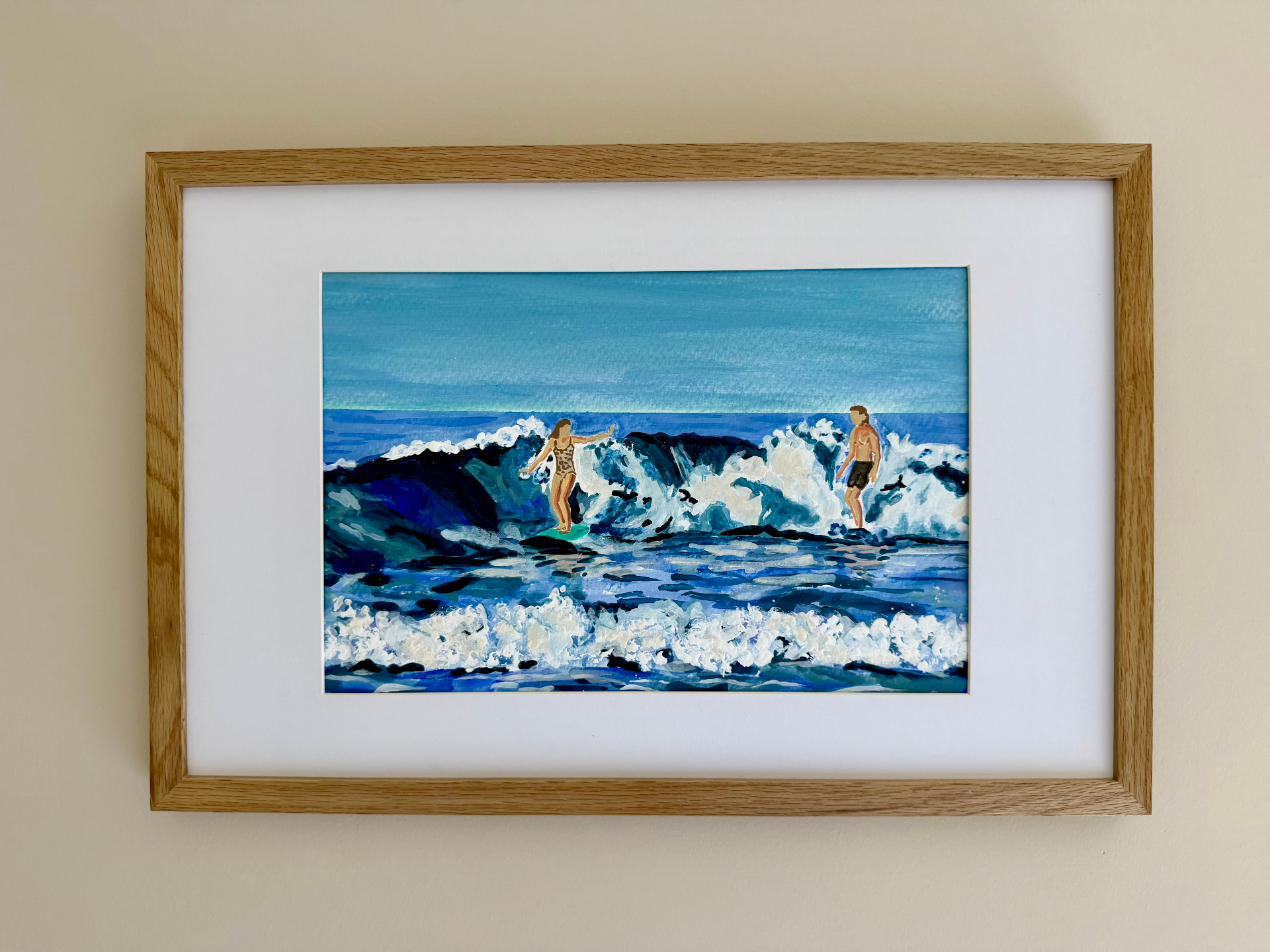 Framed watercolor of two surfers riding a cresting blue wave under an open sky