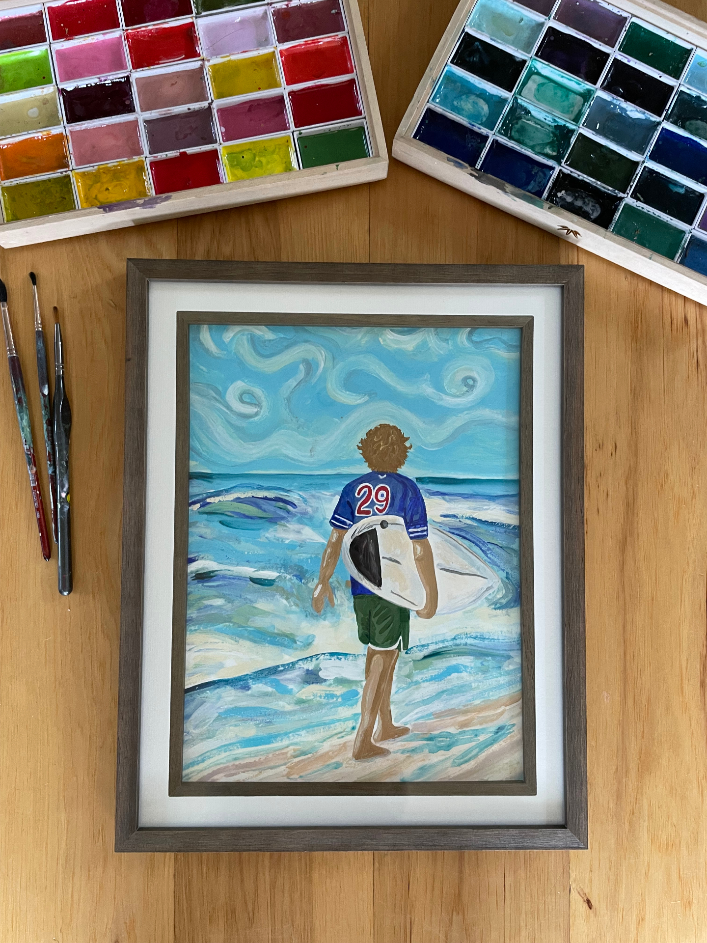 Framed painting of a young surfer in a blue jersey walking into the waves