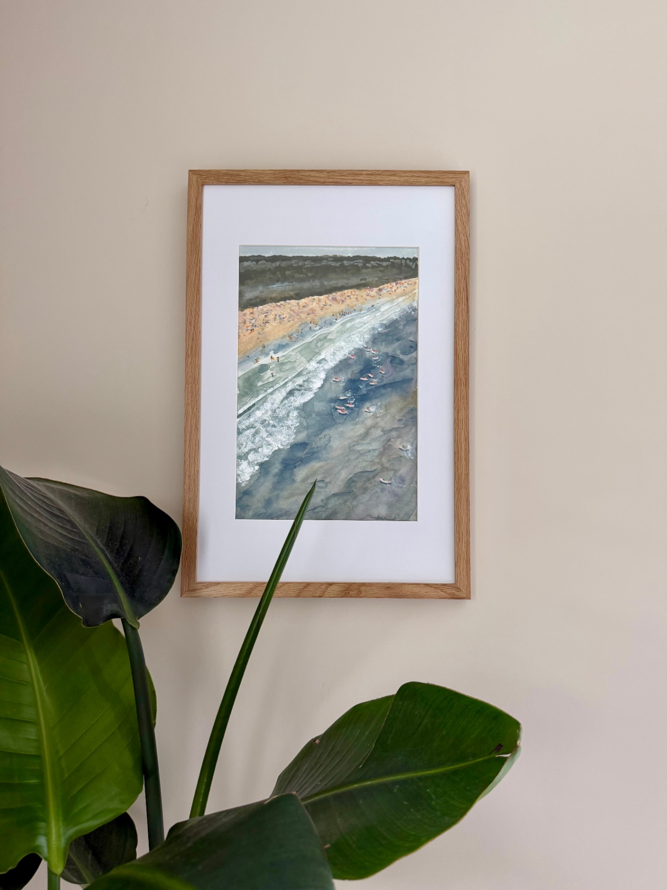 Framed aerial watercolor of a busy beach with surfers riding a soft wave