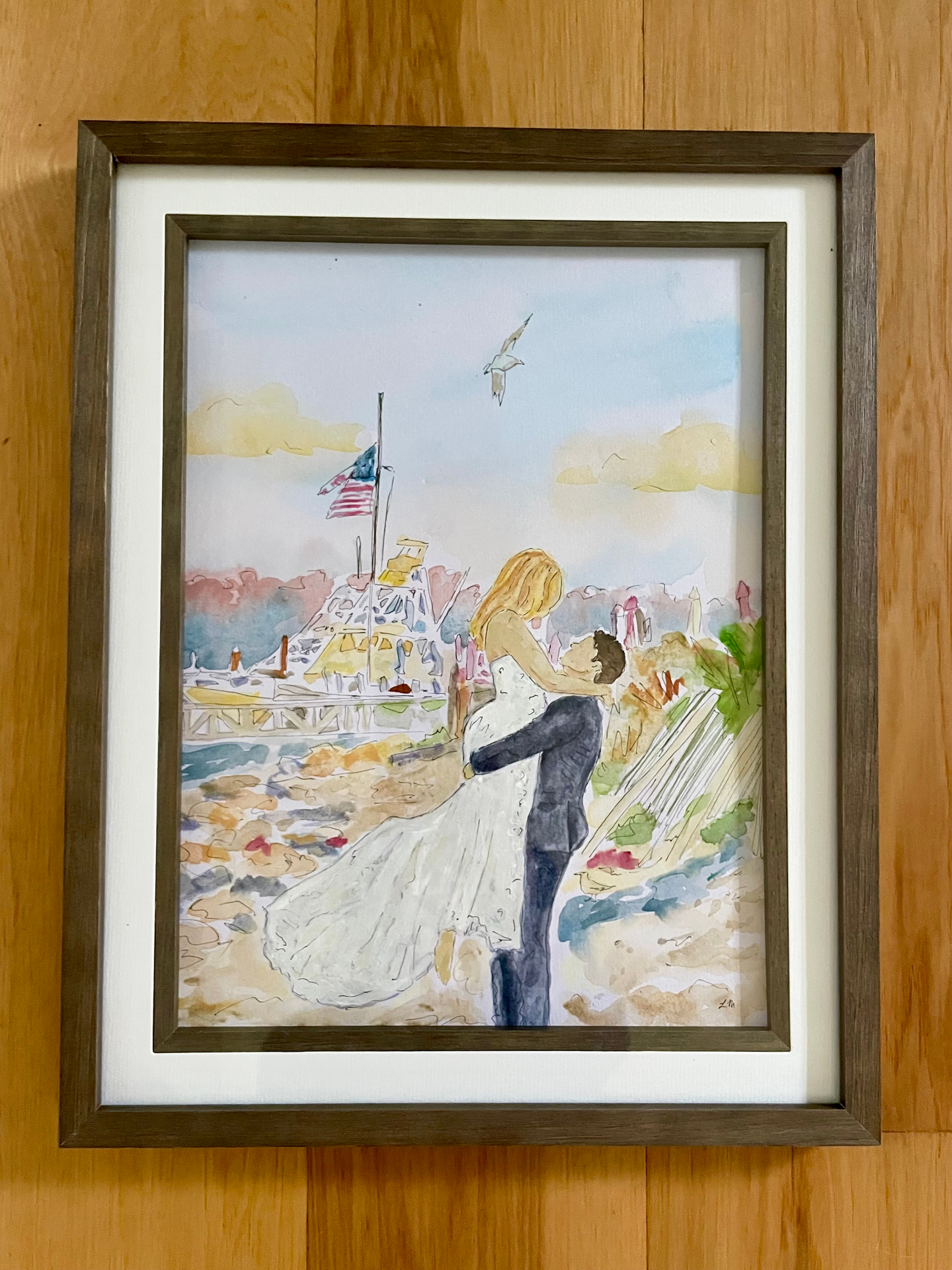 Framed watercolor of a groom lifting his bride on a New England shoreline