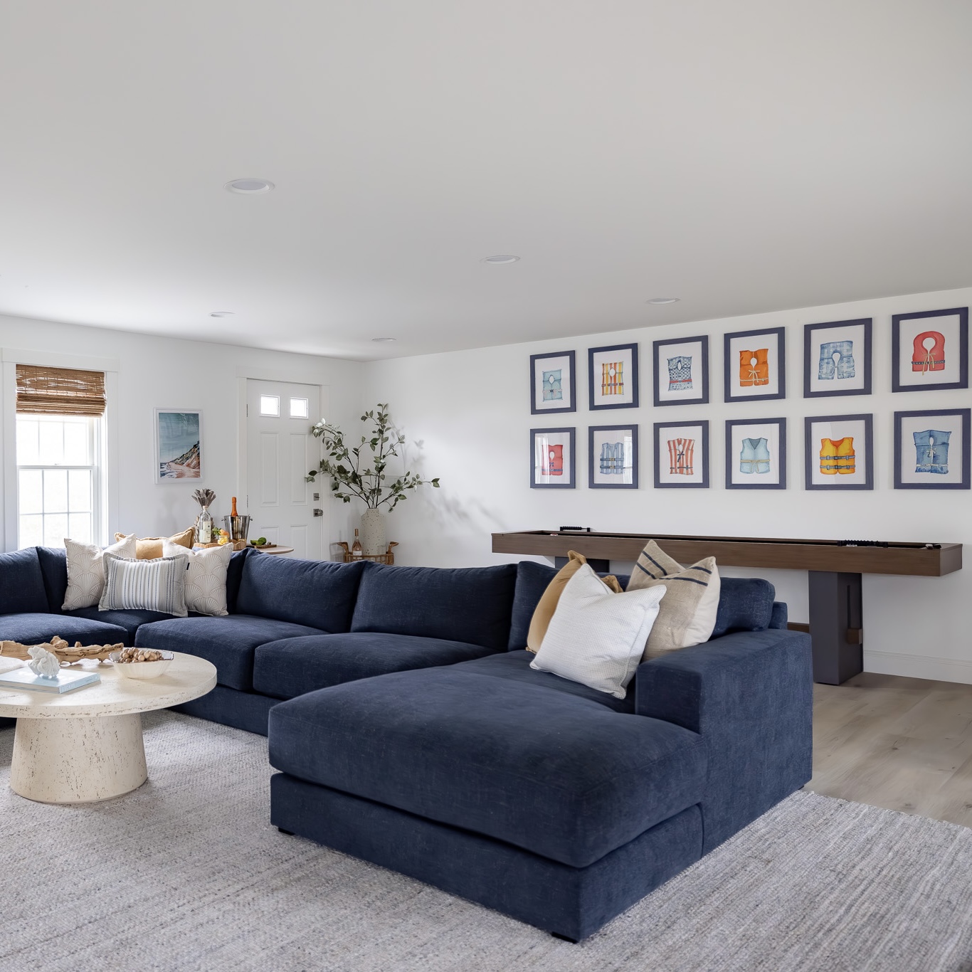 Wide view of the life vest watercolor series hung above a shuffleboard in a navy sectional lounge