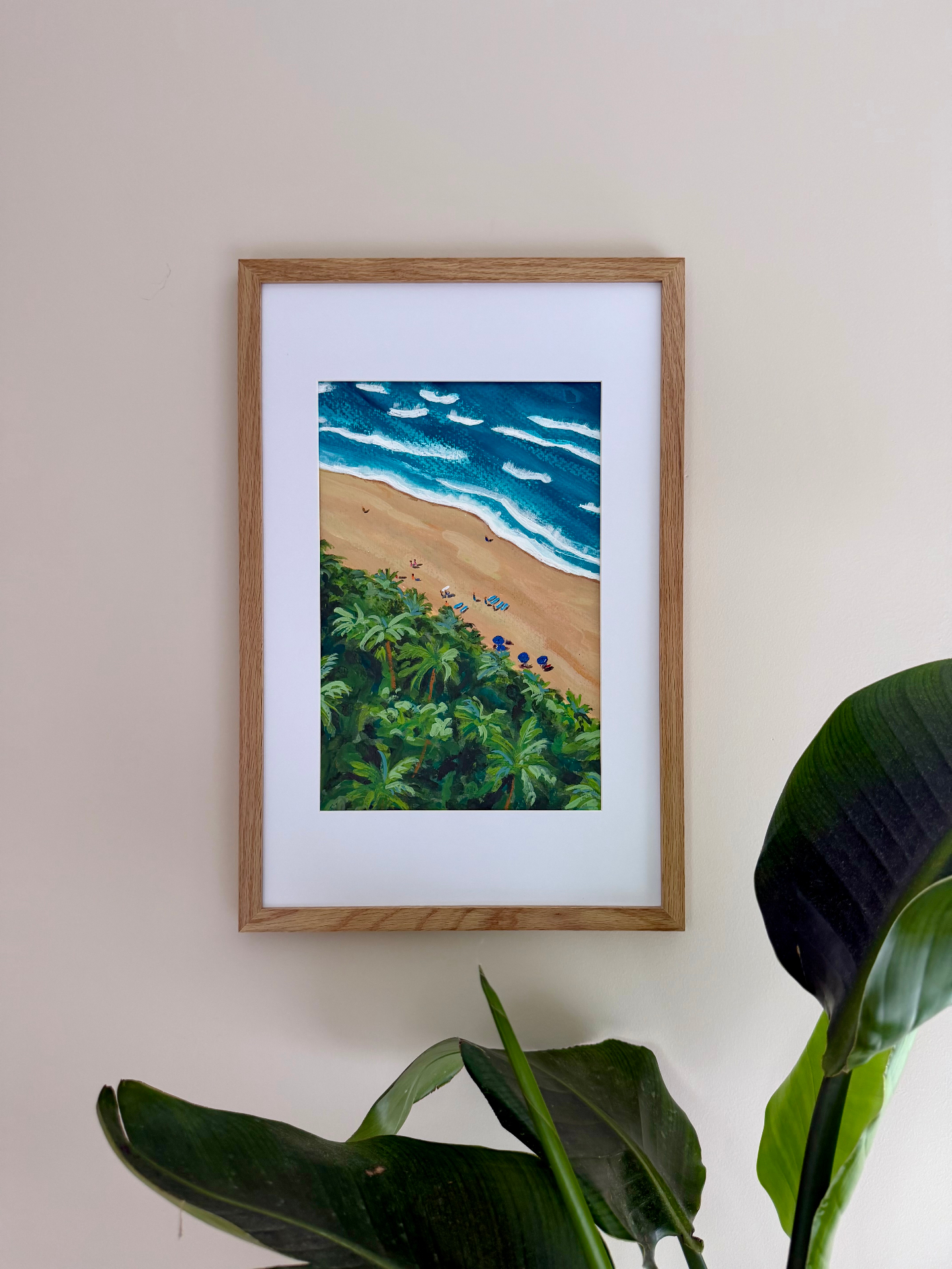 Framed aerial watercolor of a sandy beach with palm trees and blue umbrellas along the shoreline