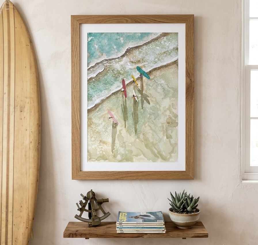 Framed watercolor of colorful surfboards lined along a pale shoreline, hung above a wood shelf