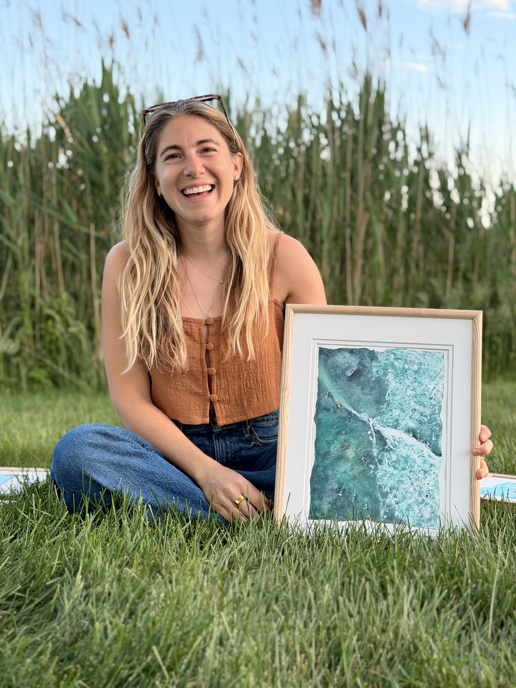 Lynn Moschella seated outdoors with a framed coastal watercolor painting